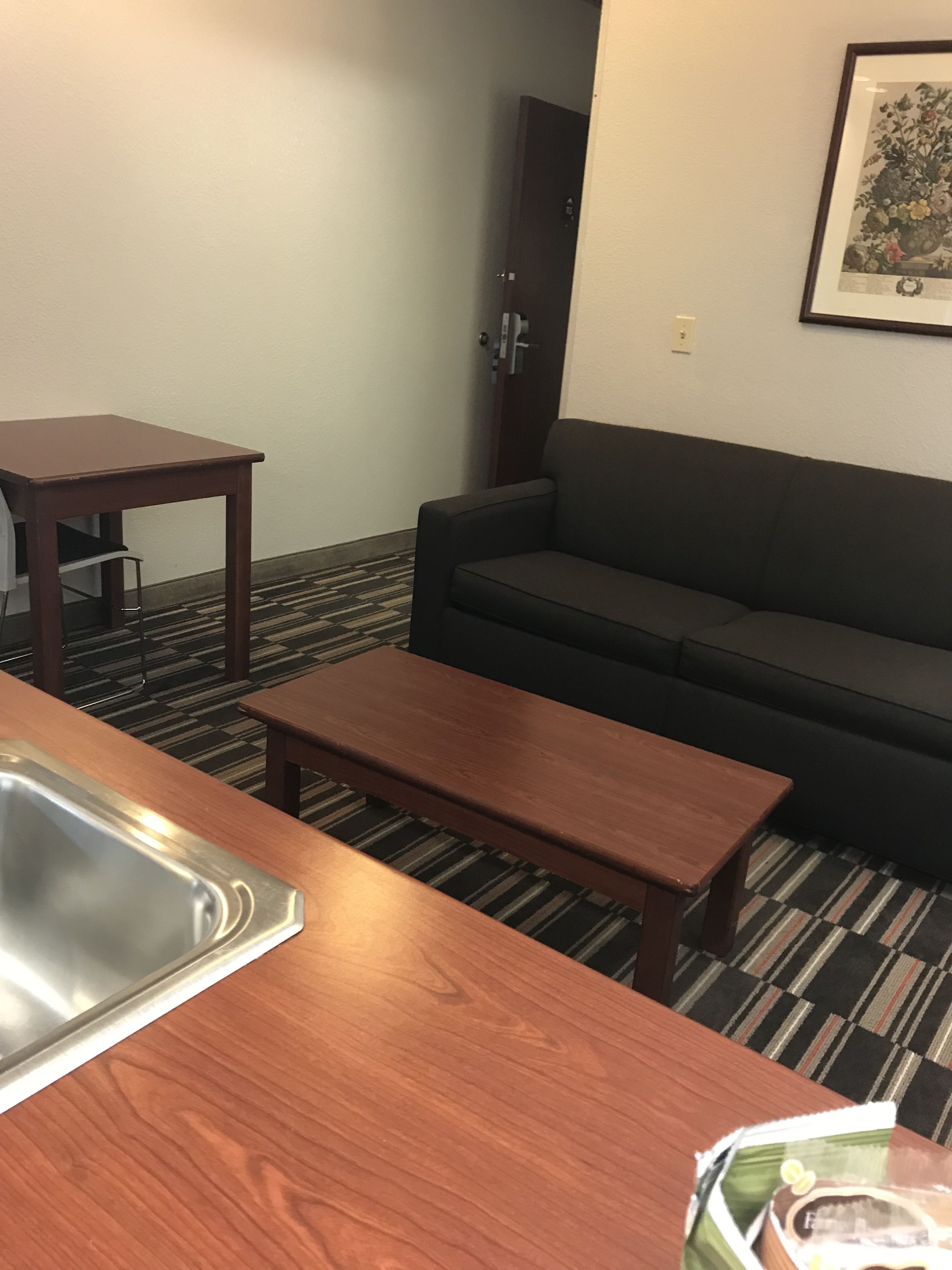 Una habitación de hotel con una mesa de madera, un sofá y un cuadro en la pared.