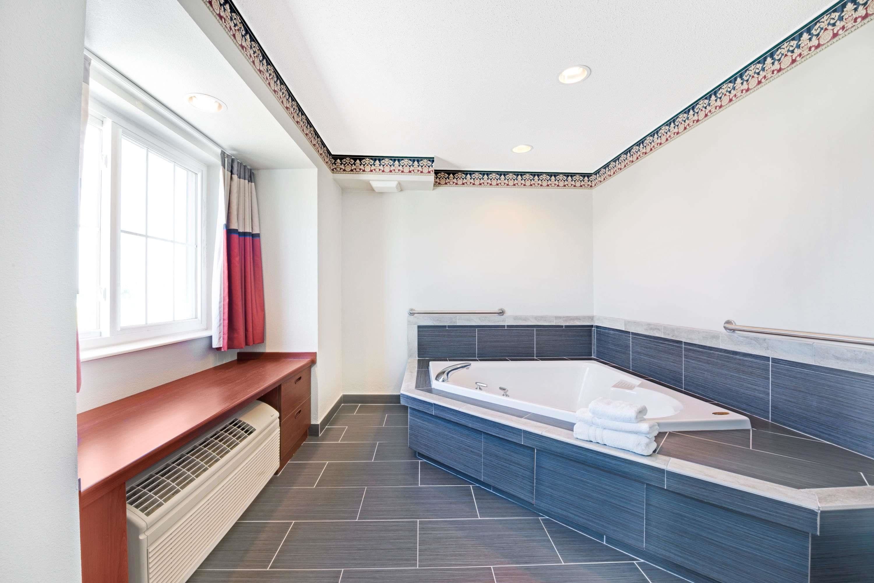 A modern bathroom with a large bathtub, a bench, and a window with curtains.