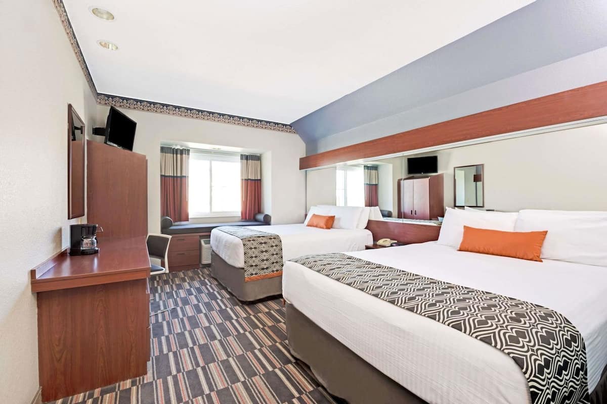 Une chambre d’hôtel équipée d’un lit, d’un bureau, d’une chaise, d’une armoire, d’une télévision et d’une fenêtre avec des rideaux.