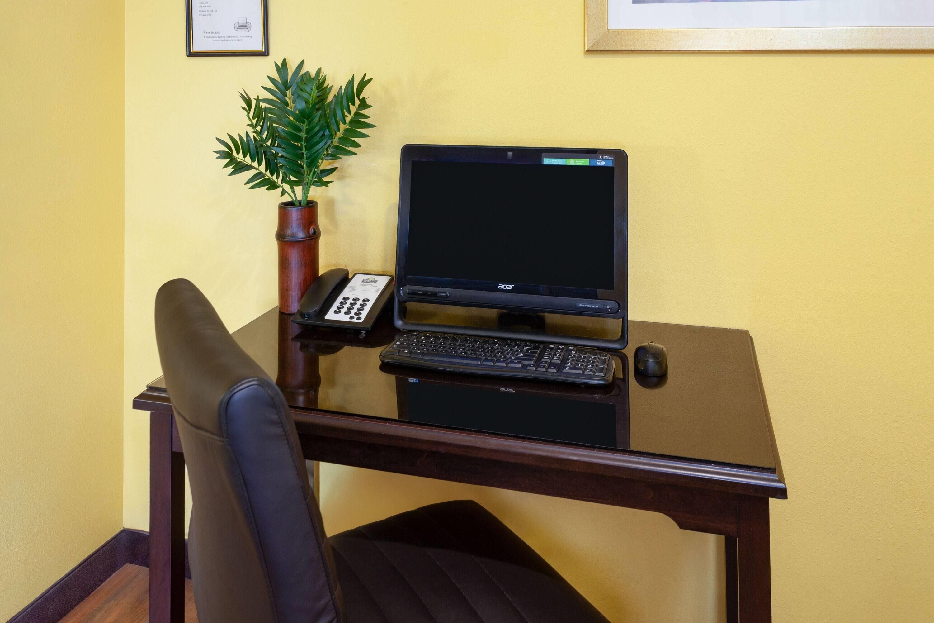 A desk with a laptop, keyboard, and phone, a chair, and a potted plant.