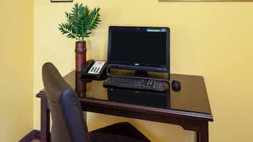 A desk with a laptop, keyboard, and phone, a chair, and a potted plant.