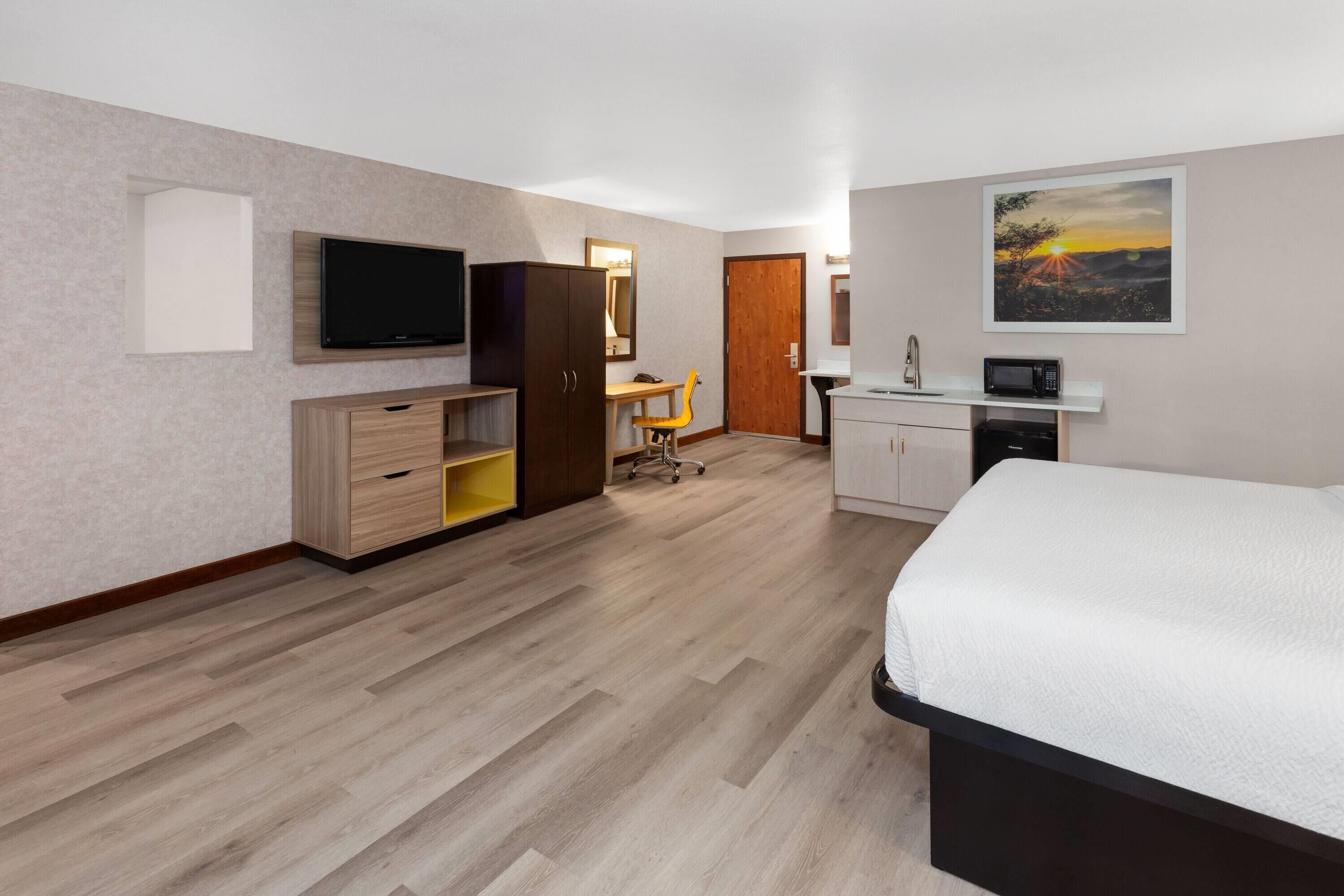 A hotel room with a bed, a desk, a television, a wardrobe, and a painting on the wall.