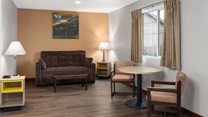 Ein Wohnzimmer mit einem braunen Sofa, einem runden Tisch mit zwei Stühlen, einer Lampe und einem Gemälde an der Wand.