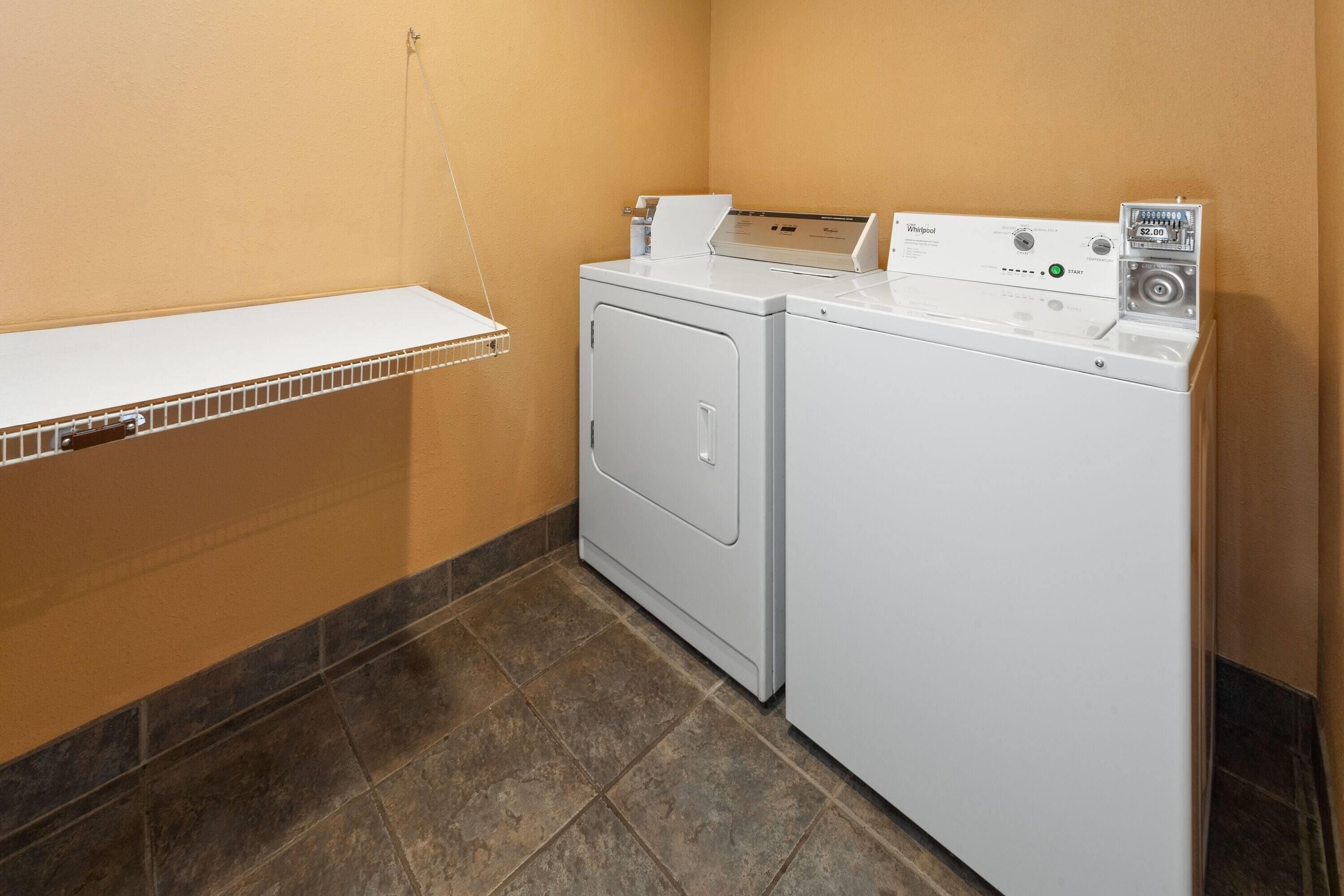 A laundry area with a white washer and dryer, a metal shelf, and a tiled floor.
