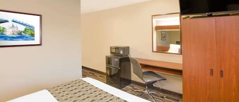 A hotel room with a bed, a desk, a chair, a wardrobe, a television, and a framed picture on the wall.