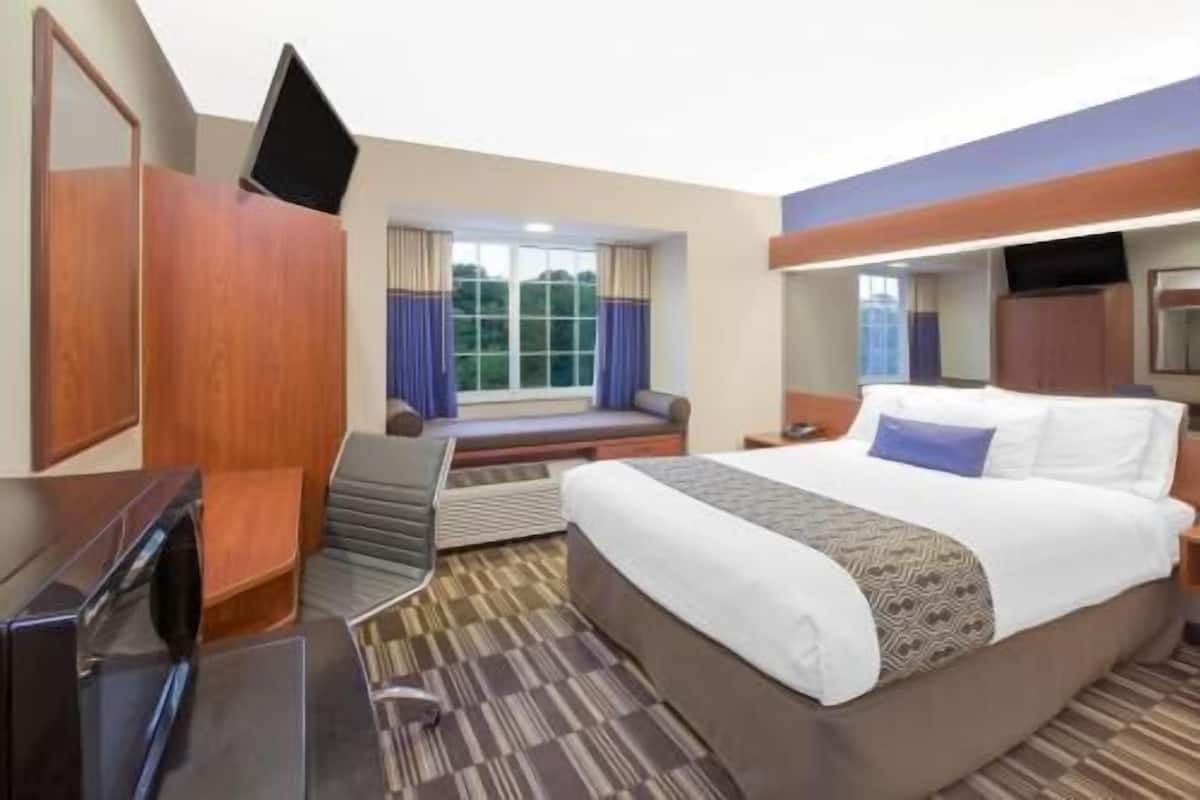 A hotel room with a bed, a desk, a chair, a TV, and a window with curtains.