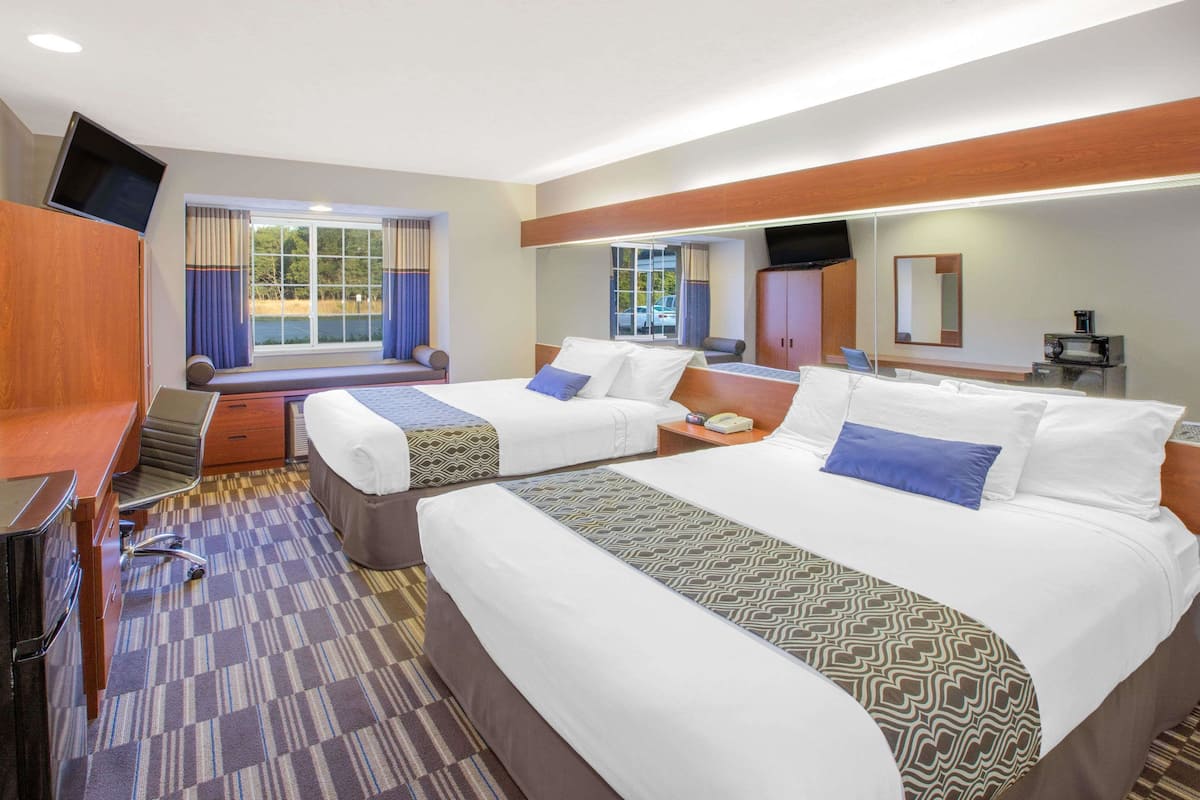 A hotel room with two beds, a desk, a chair, a TV, and a large window with curtains.