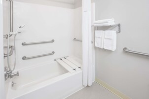 Un baño moderno con bañera, barras de apoyo, toallero y cabezal de ducha.