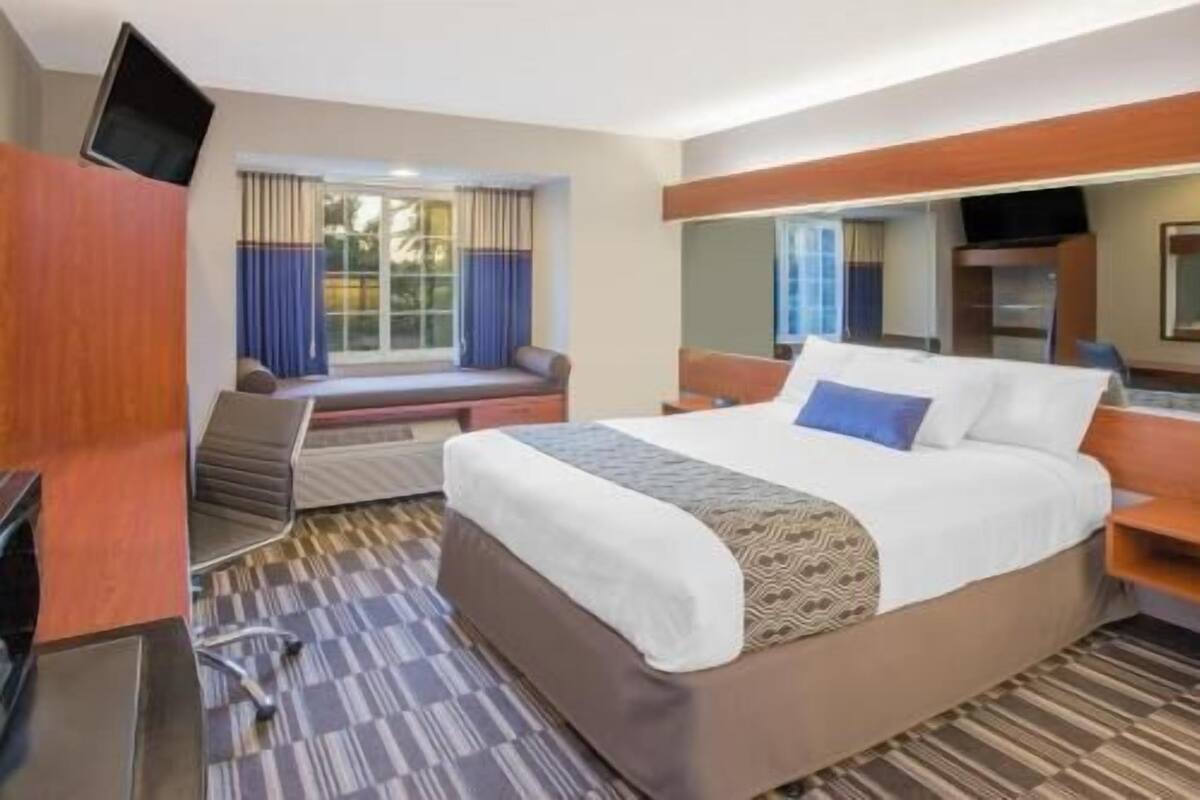 A hotel room with a bed, a desk, a chair, a TV, and a window with curtains.
