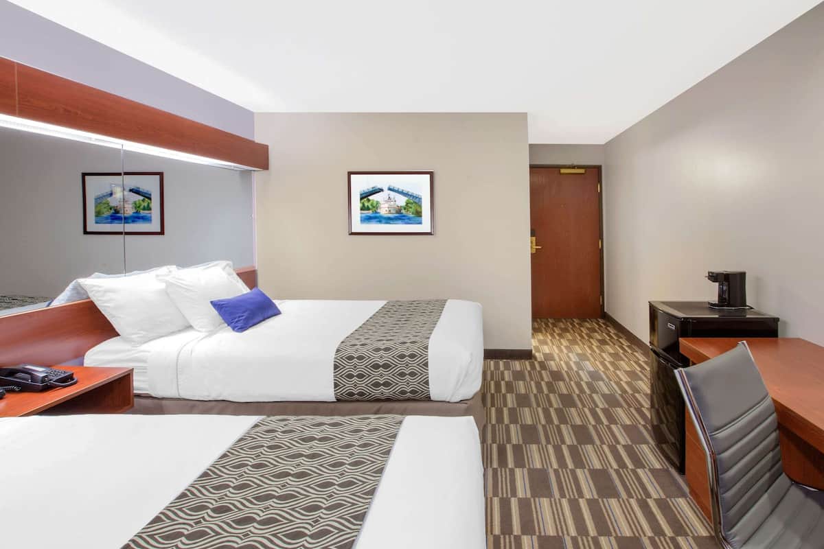 A hotel room with two beds, a desk, a chair, a coffee machine, and two framed pictures on the wall.