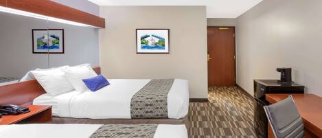 A hotel room with two beds, a desk, a chair, a coffee machine, and two framed pictures on the wall.