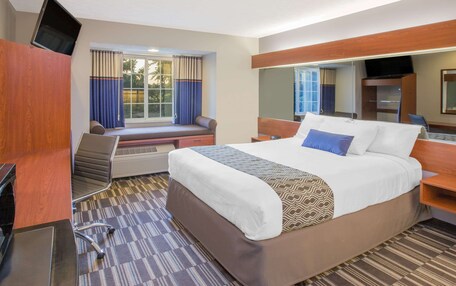 A hotel room with a large bed, a desk, a chair, a television, and a window with curtains.