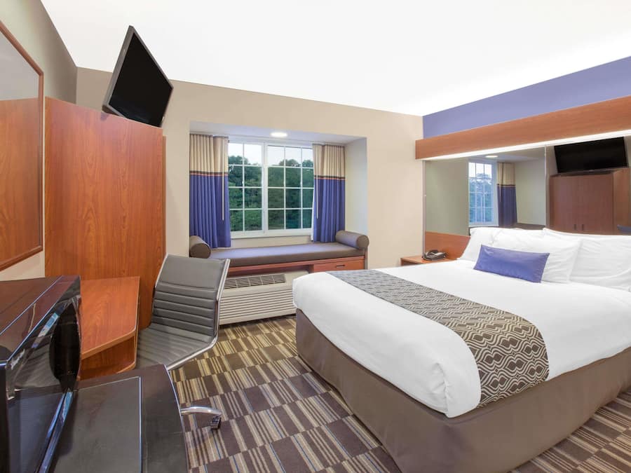 Quarto de hotel com uma cama grande, uma mesa de escritório com televisão de tela plana, área de estar com vista para o exterior e uma janela com cortinas.