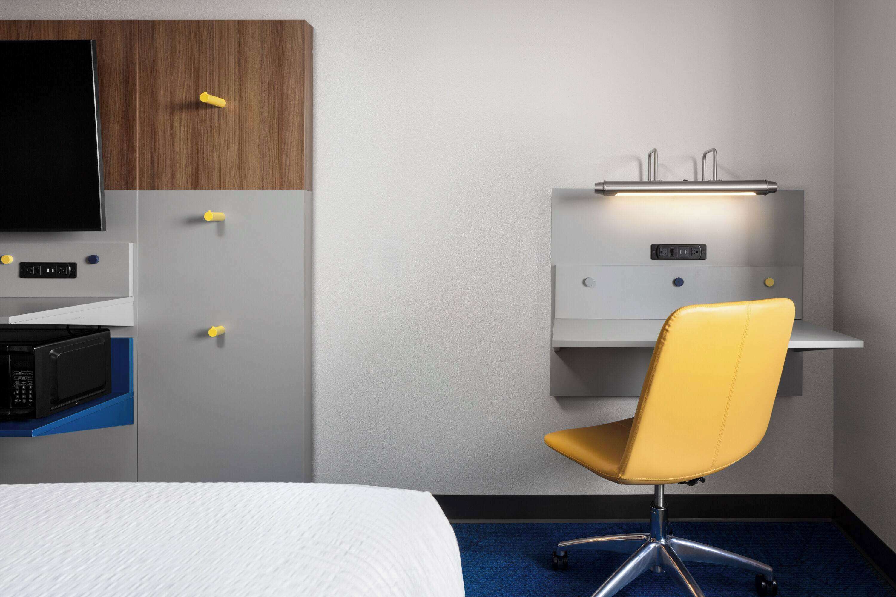 Ein Hotelzimmer mit Bett, Schreibtisch mit Computer, Stuhl, Mikrowelle und Fernseher.