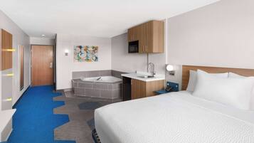 Una habitación de hotel con una cama grande, un baño con bañera, lavamanos y microondas.