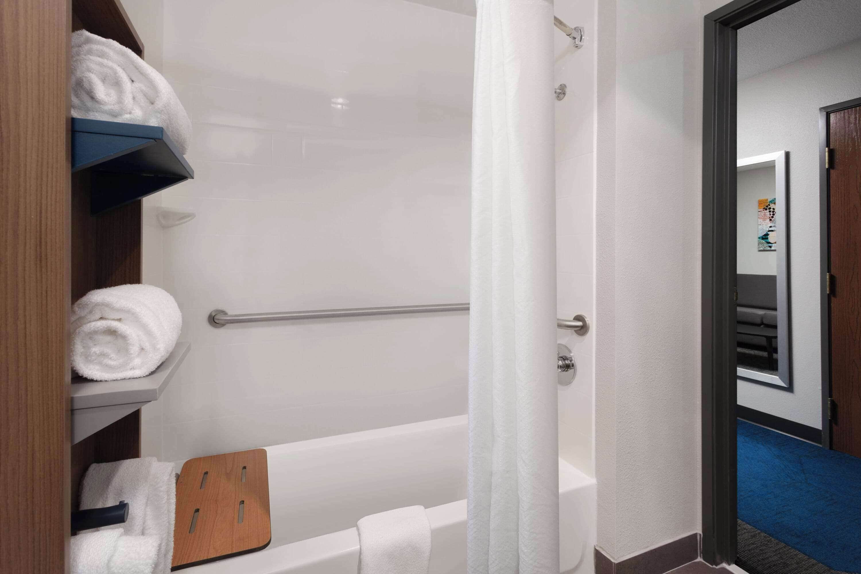 A bathroom with a bathtub, a towel rack, and a wooden shelf with towels.