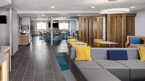 Un moderno hall de hotel con una zona de estar, una recepción y una cocina al fondo.
