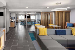 Un hall d’hôtel moderne avec un espace salon, un comptoir d’accueil et une cuisine en arrière-plan.