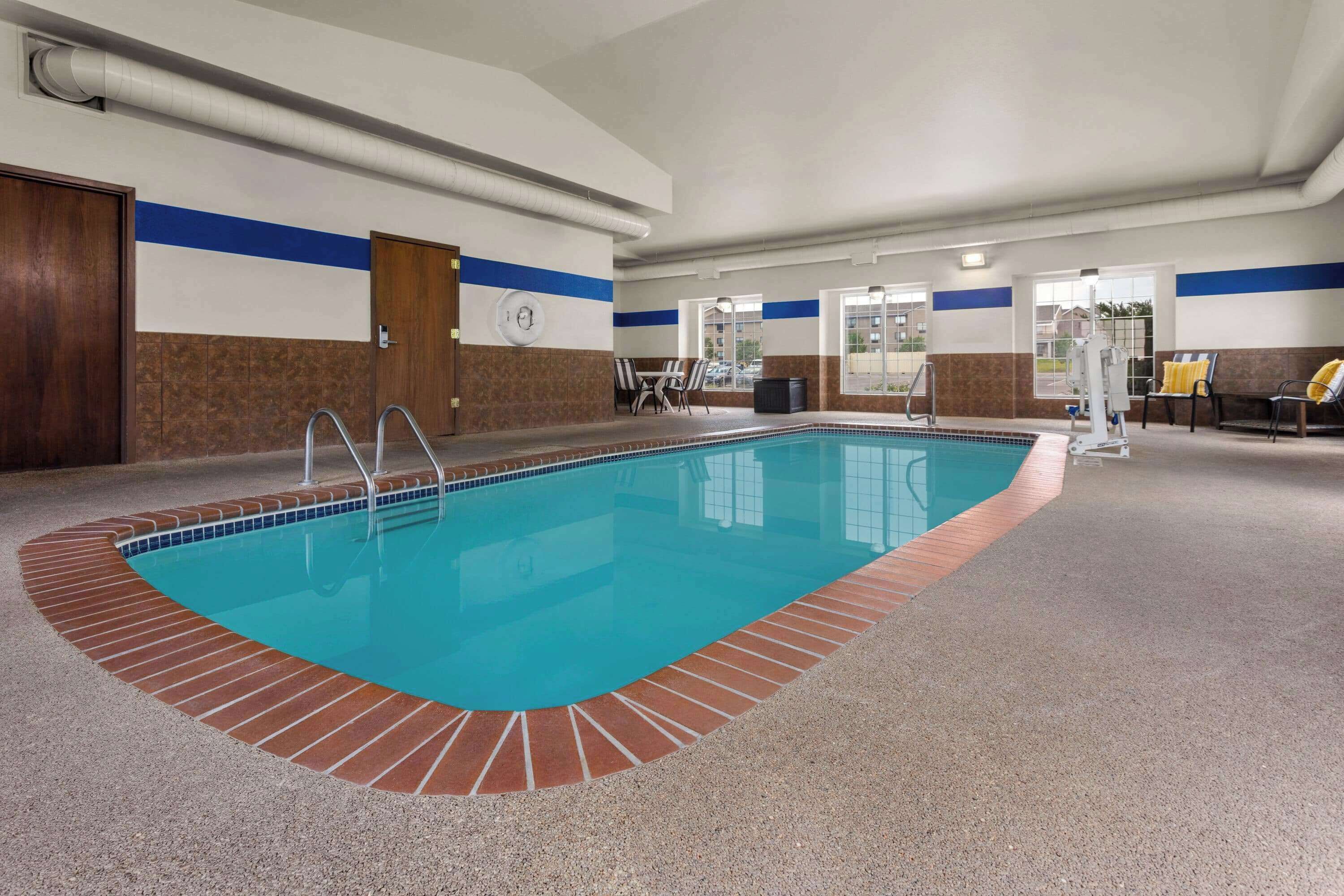An indoor swimming pool with a tiled edge, a clock on the wall, and a view of the outside through large windows.
