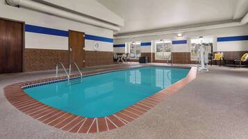 An indoor swimming pool with a tiled edge, a clock on the wall, and a view of the outside through large windows.