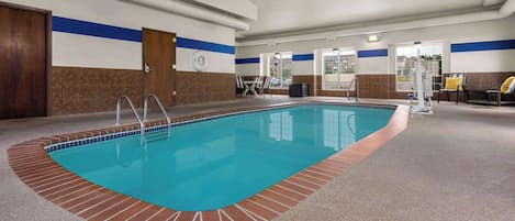 An indoor swimming pool with a tiled edge, a clock on the wall, and a view of the outside through large windows.