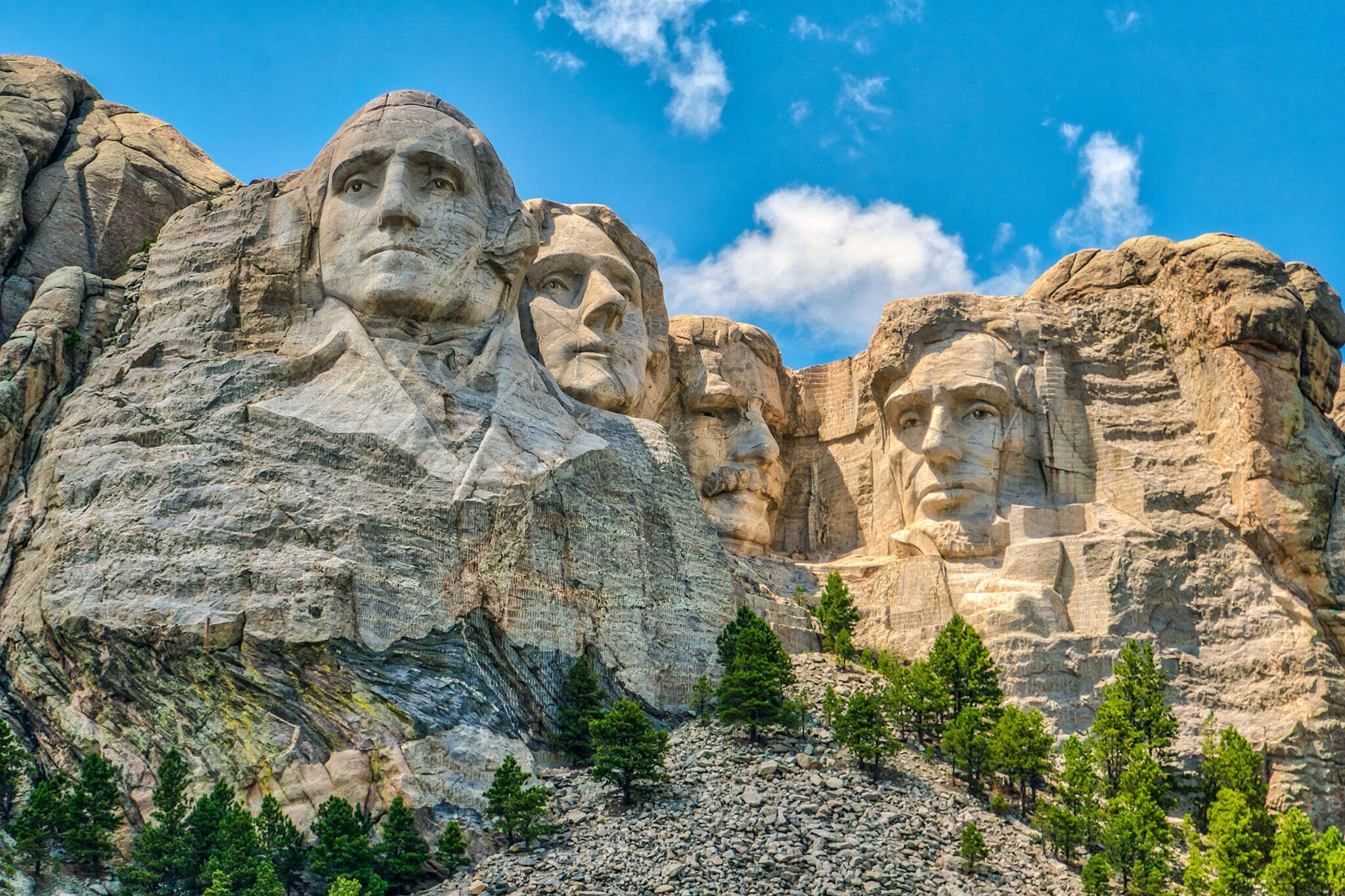A large mountain with carved faces, surrounded by rocky terrain and sparse vegetation.