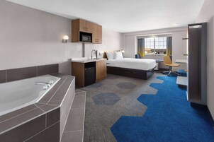 Une chambre d’hôtel moderne dotée d’une grande baignoire, d’une chambre séparée avec un lit et un bureau, d’une petite kitchenette et d’une vue sur la ville.