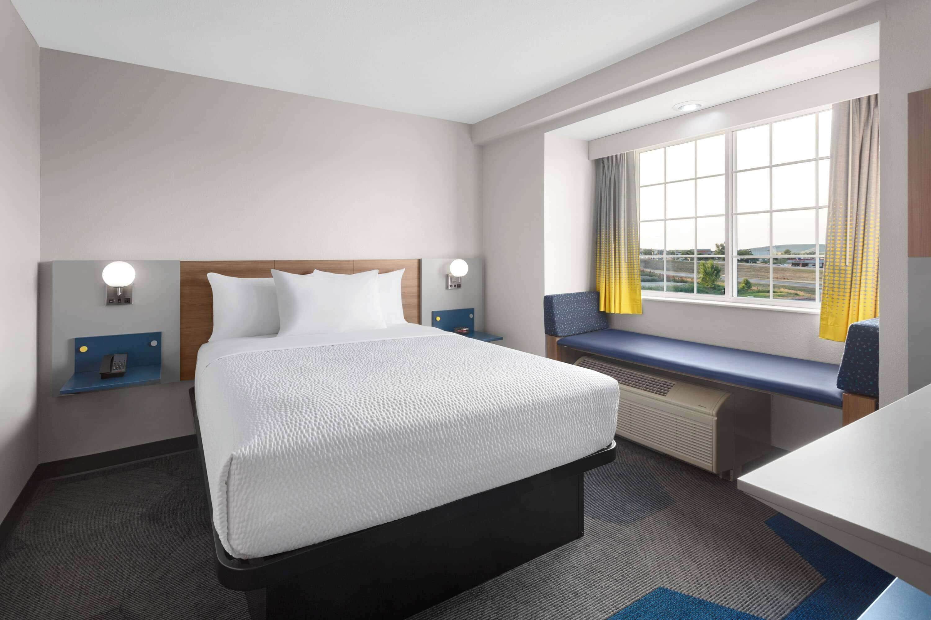 Een hotelkamer met een groot bed, een bureau, een raam met gordijnen en uitzicht op buiten.