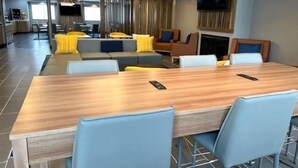Una habitación de hotel moderna con una mesa de comedor de madera, sillas azules y un sofá con cojines amarillos.