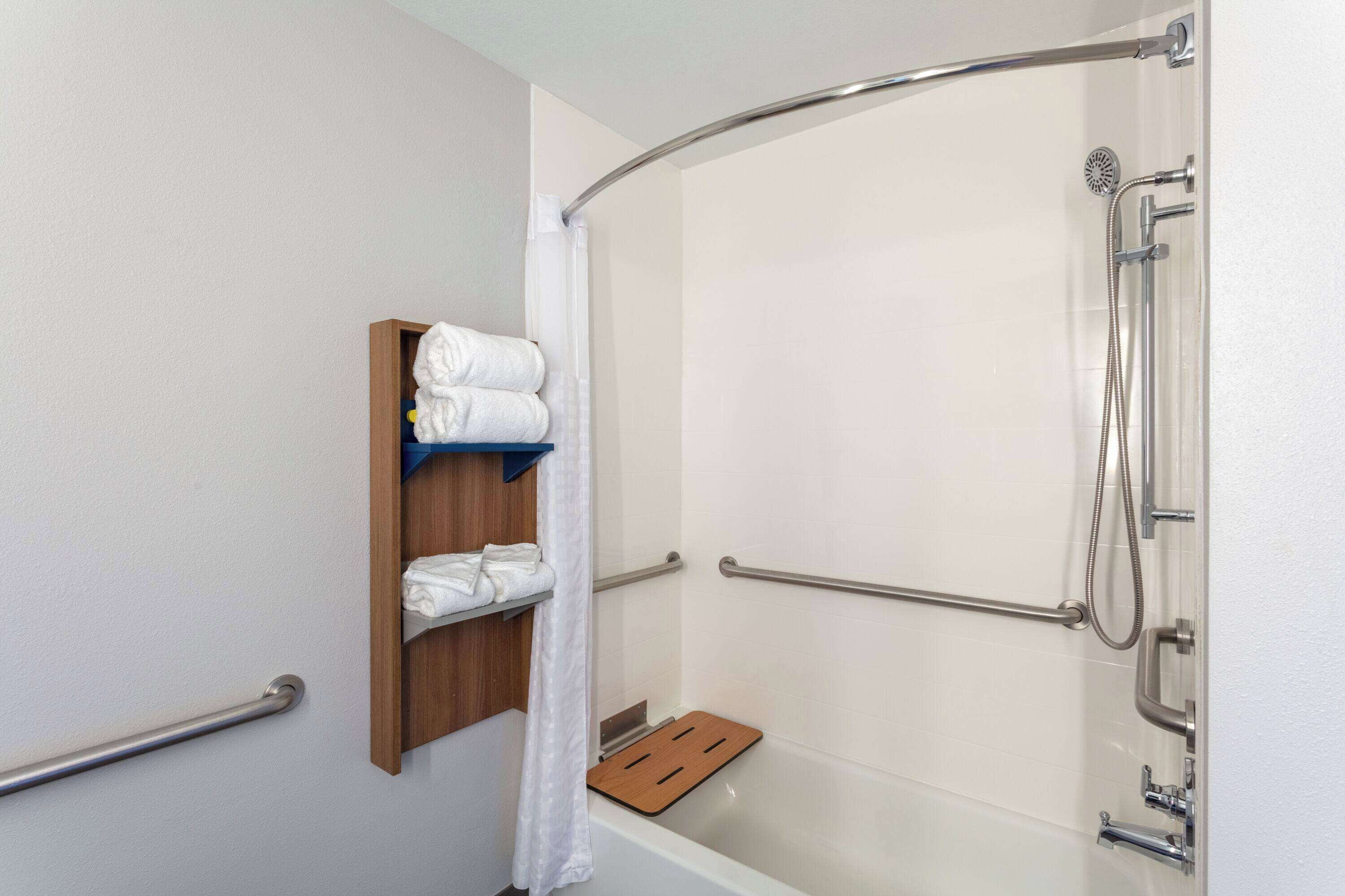 A shower area with a grab bar, a shelf with towels, and a showerhead.
