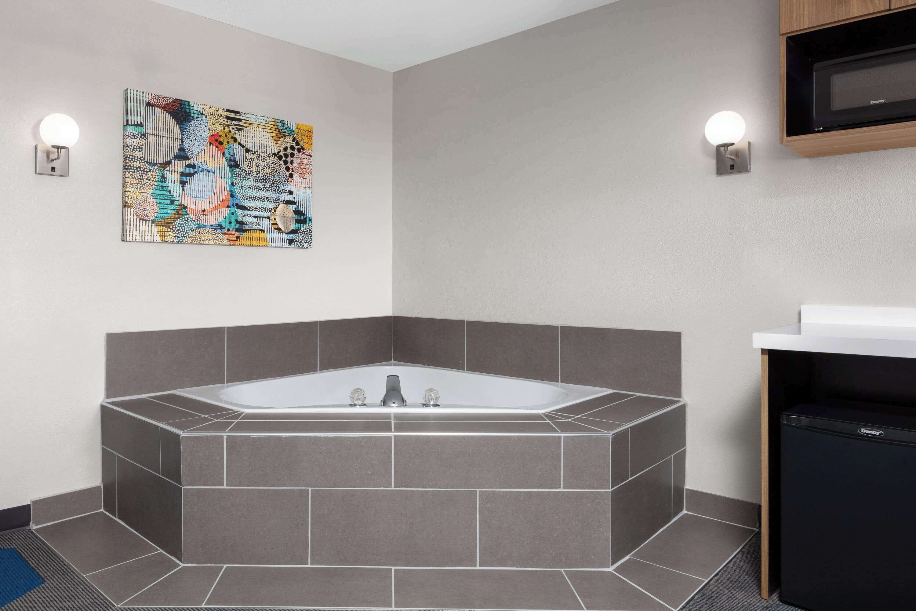 Un baño moderno con una bañera independiente, un cuadro abstracto colgado en la pared y un microondas integrado.
