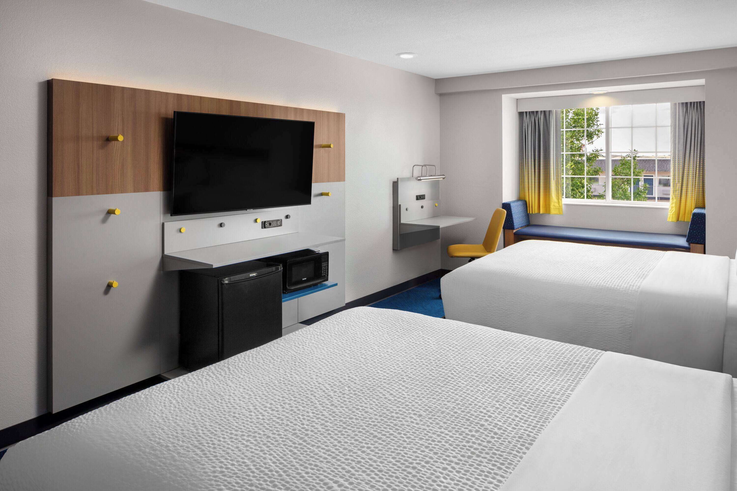 Habitación de hotel con dos camas, televisión, microondas, escritorio pequeño y ventana con cortinas.