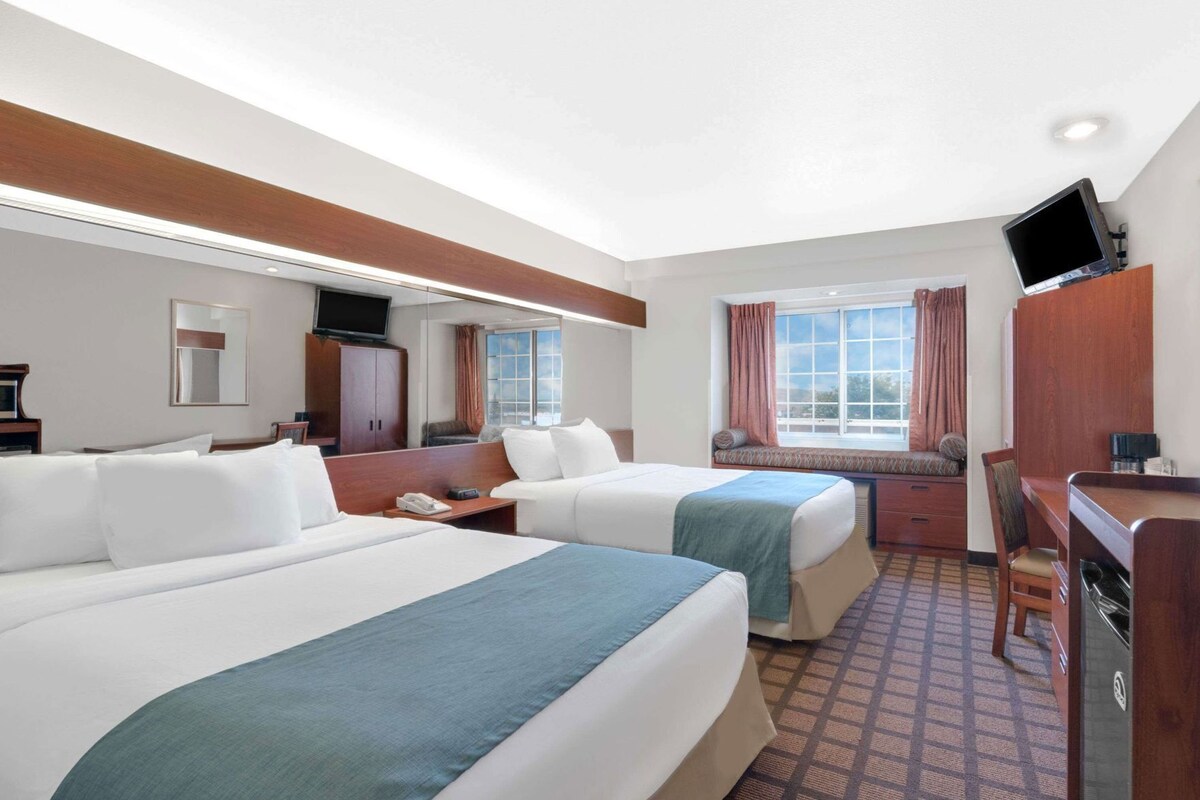 A hotel room with two beds, a desk, a chair, a TV, and a window with curtains.