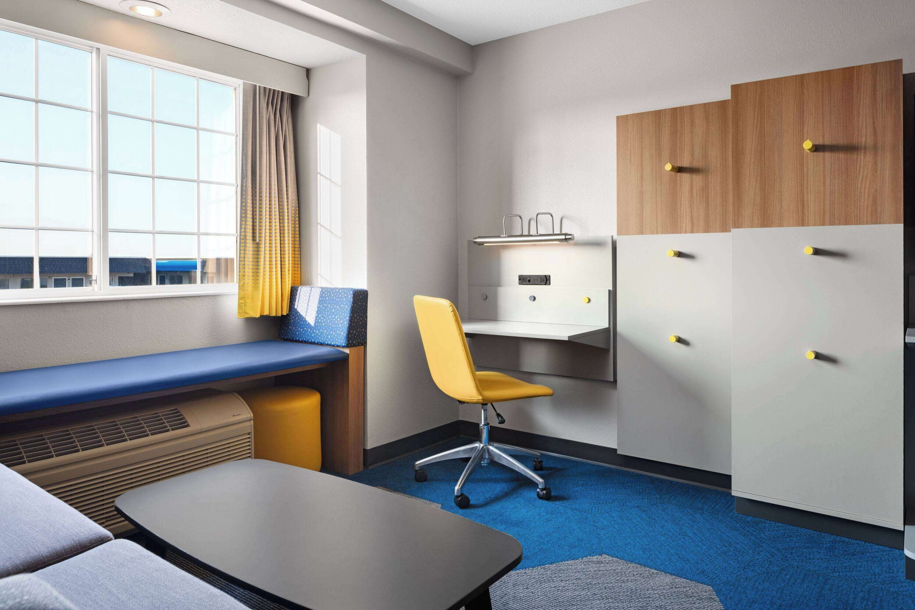 A hotel room with a desk, chair, and a bed.