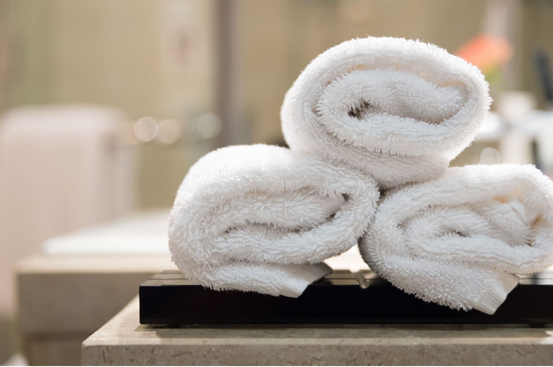 Three rolled white towels stacked on a black tray.