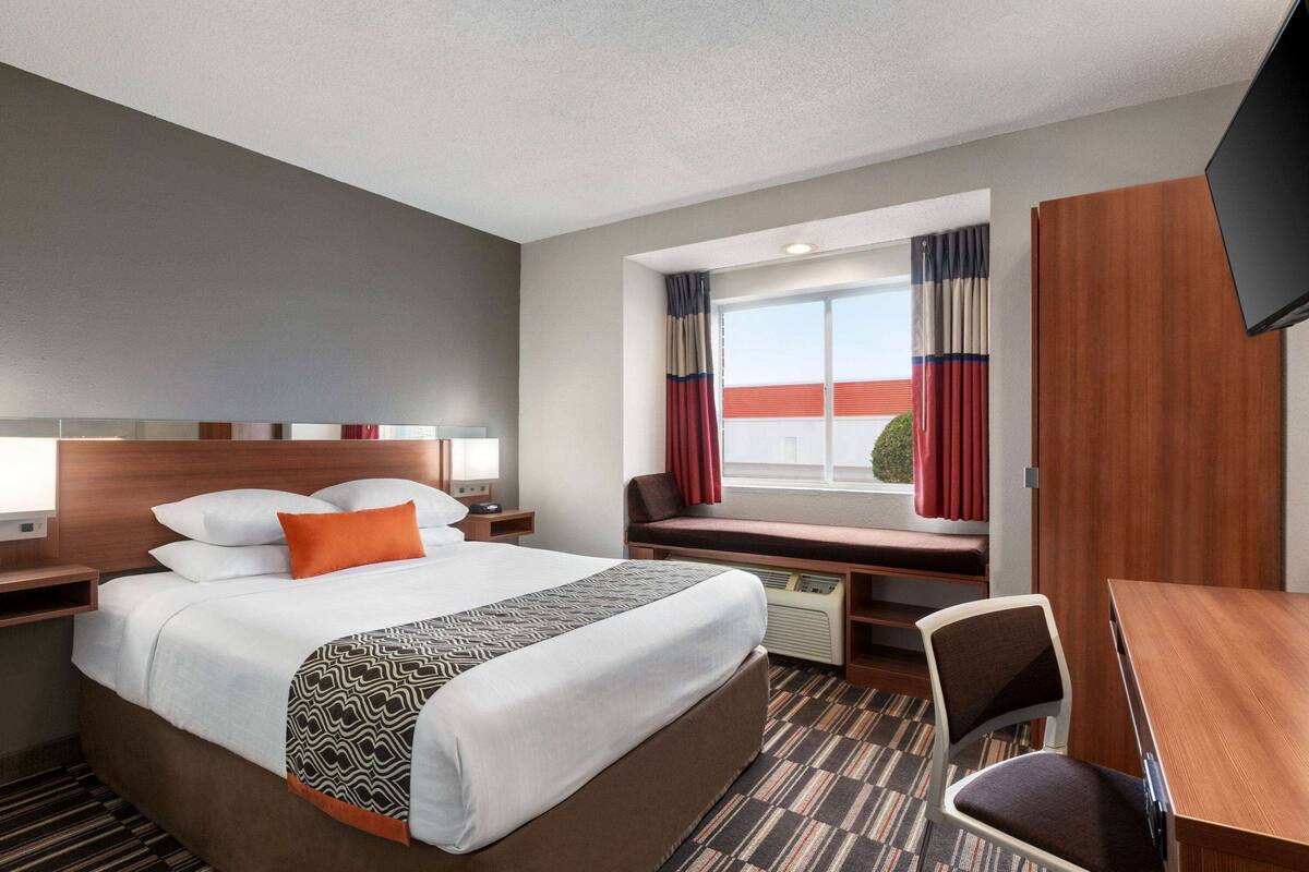 A hotel room with a large bed, a desk, a chair, a TV, and a window with curtains.