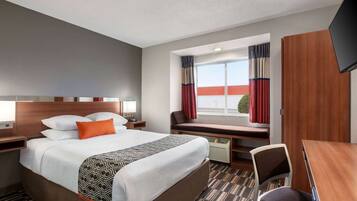 Habitación de hotel con una cama grande, un escritorio, una silla, un televisor y una ventana con cortinas.