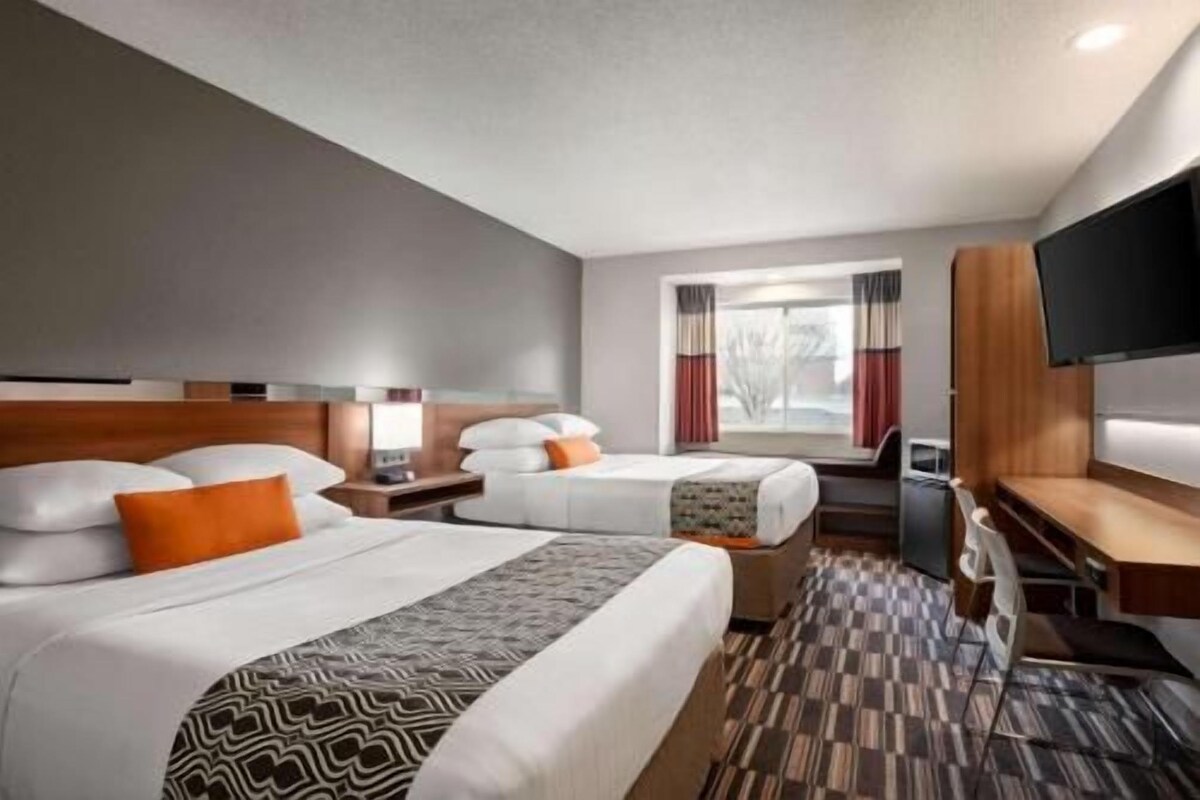 A hotel room with two beds, a TV, a desk, and a window with curtains.