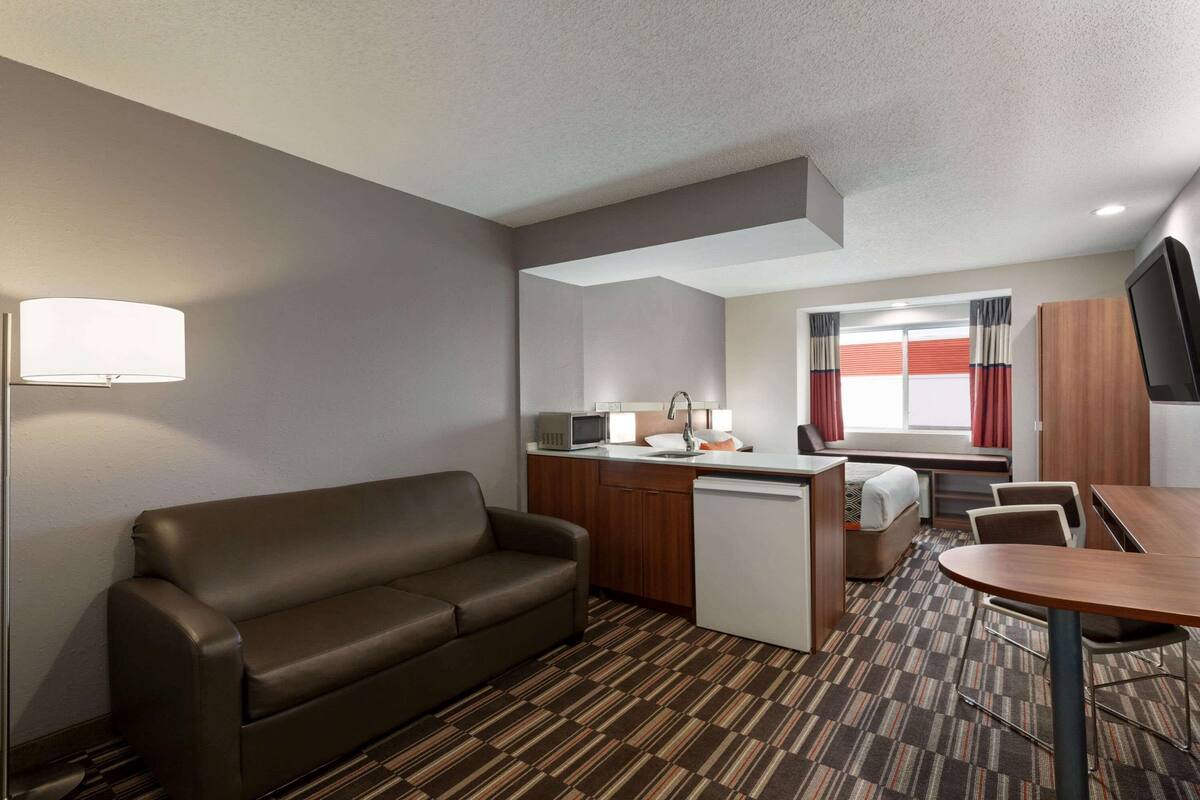 A compact hotel room with a sofa, kitchenette, dining area, and a bed.