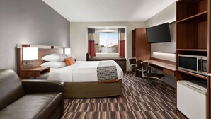 A hotel room with a bed, a desk, a chair, a TV, and a minibar. - Microtel Inn & Suites by Wyndham Tifton (Tifton)