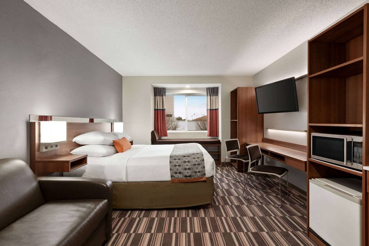 A hotel room with a bed, a desk, a chair, a TV, and a minibar.