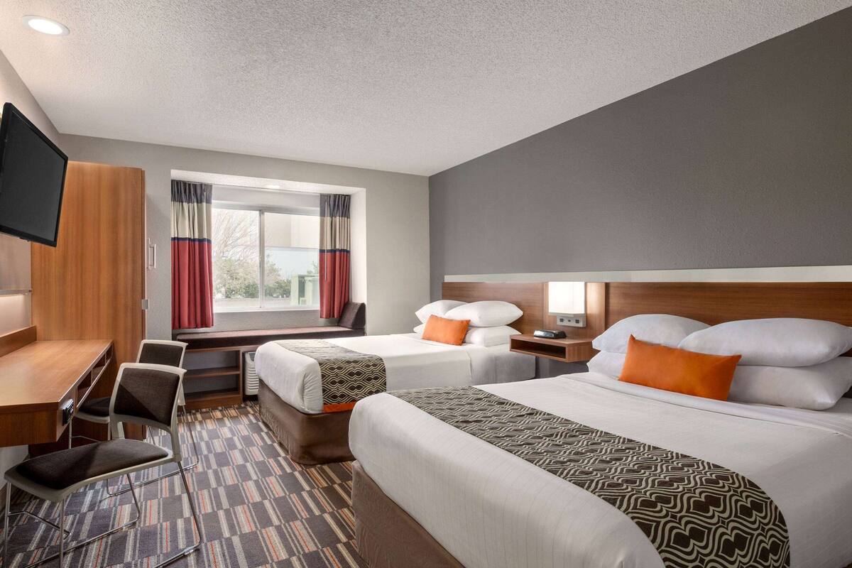 A hotel room with two beds, a desk, a chair, a TV, and a window with curtains.