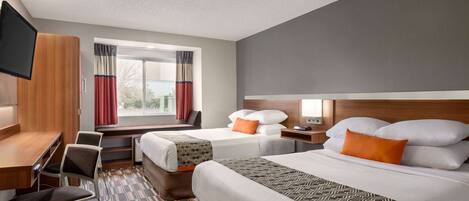A hotel room with two beds, a desk, a chair, a TV, and a window with curtains.