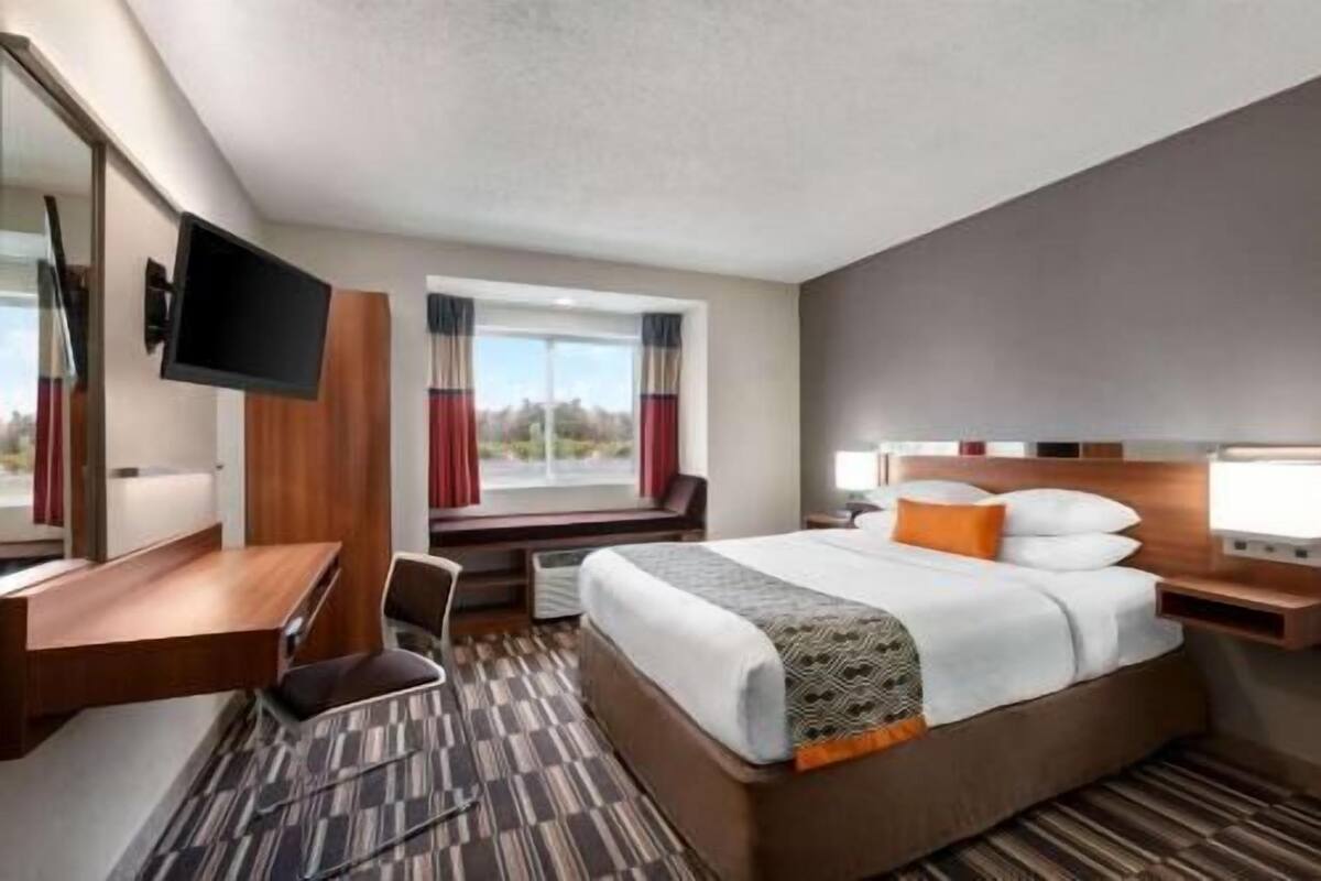 A hotel room with a bed, a desk, a chair, a TV, and a window with curtains.