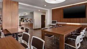A modern conference room with a large wooden table, white chairs, a flat-screen TV, and a kitchen area in the background. - Microtel Inn & Suites by Wyndham Tifton (Tifton)