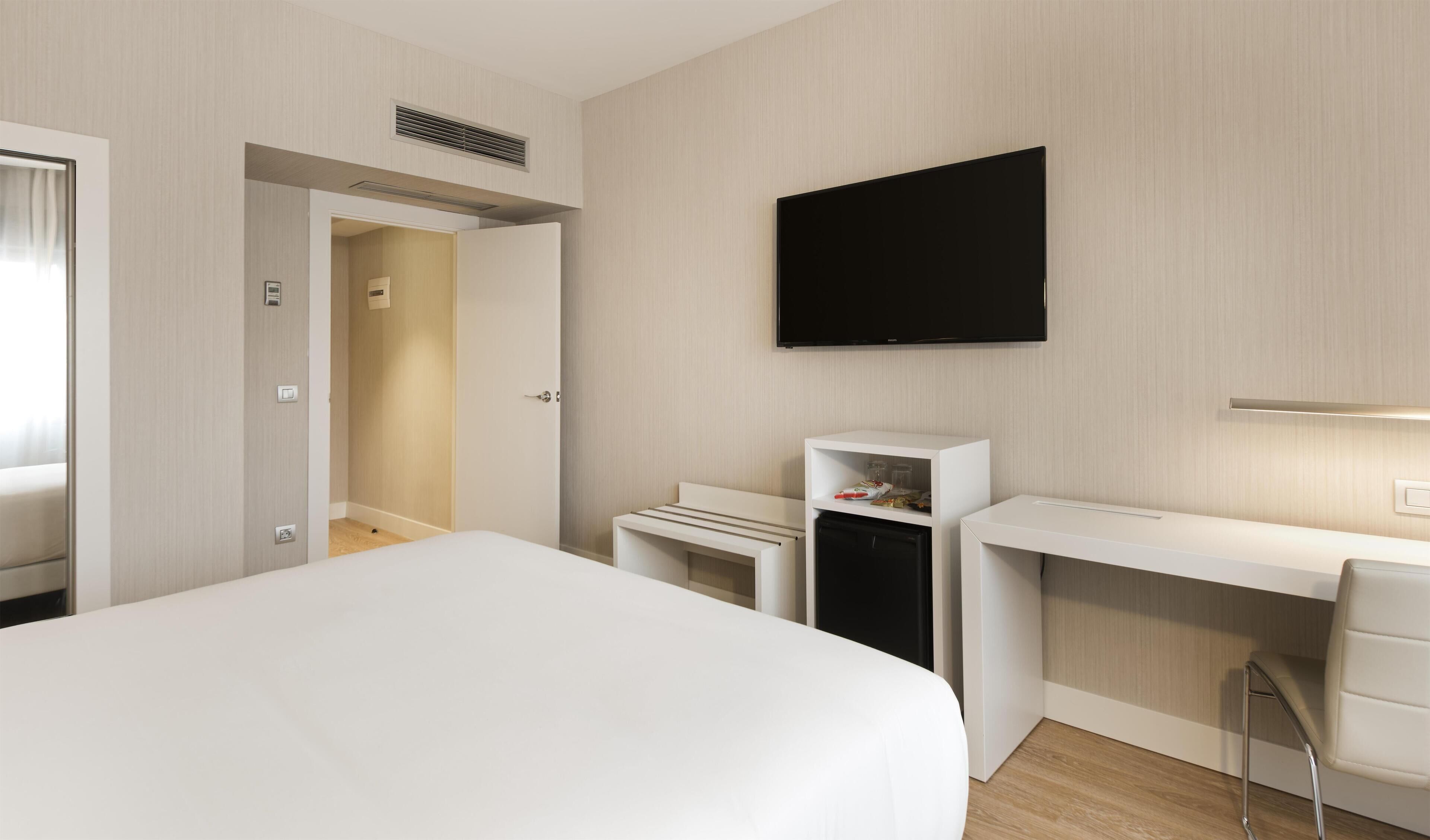 A hotel room with a bed, a desk, a chair, a TV, and a wardrobe.