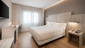 A modern hotel room with a large bed, a desk, and a TV mounted on the wall.
