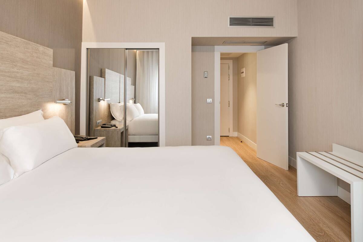 Moderni hotellihuone, jossa on suuri sänky, yöpöydät, televisio ja erillinen vaatehuone.