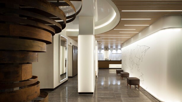 A modern lobby with a central spiral staircase, a reception desk, and a wall with abstract art.