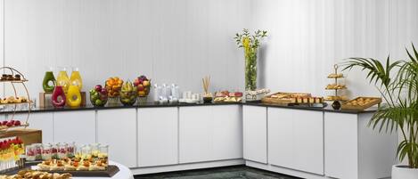 Un buffet est installé sur une table blanche, avec divers plats et boissons, le tout placé devant un mur blanc.